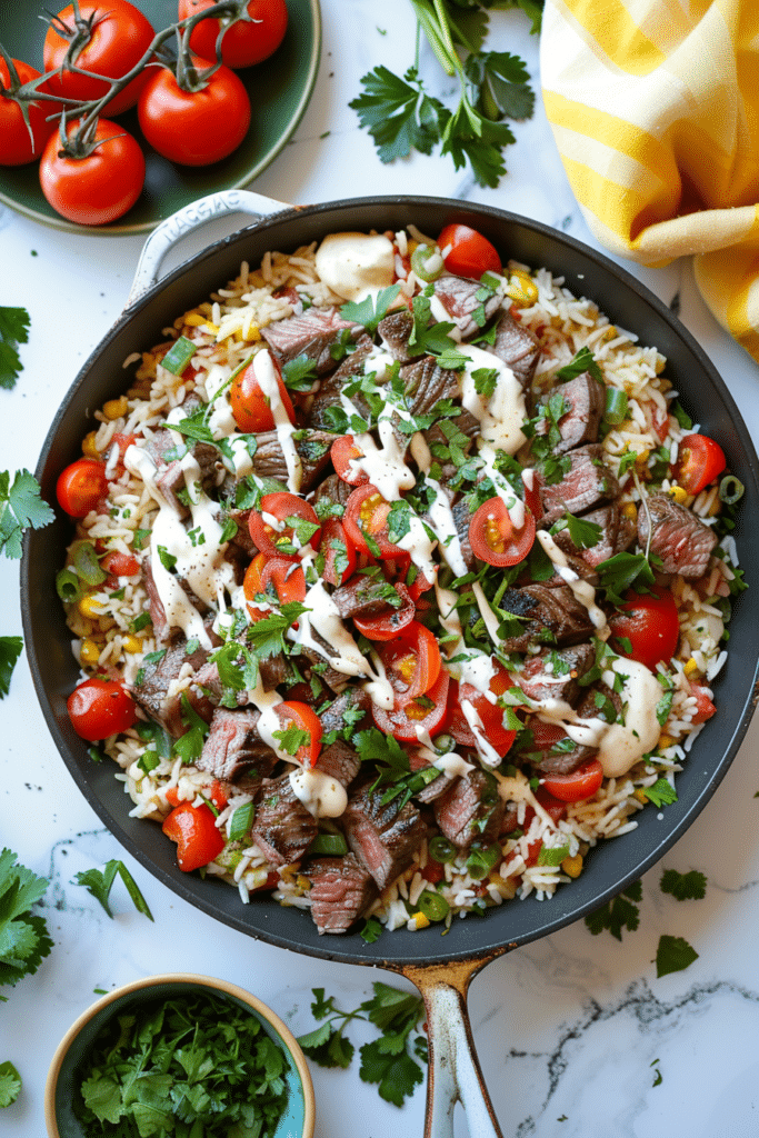 Skillet filled with Steak & Queso Rice, topped with creamy queso sauce and tomato rice, surrounded by fresh tomatoes, parsley, and colorful kitchen napkins on a white marble background