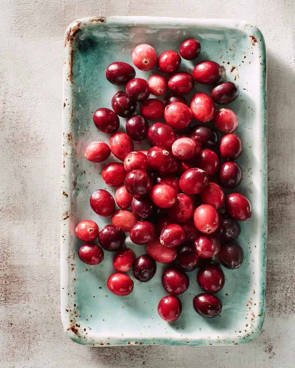 Fresh cranberries scattered on a rustic seafoam tray with natural lighting