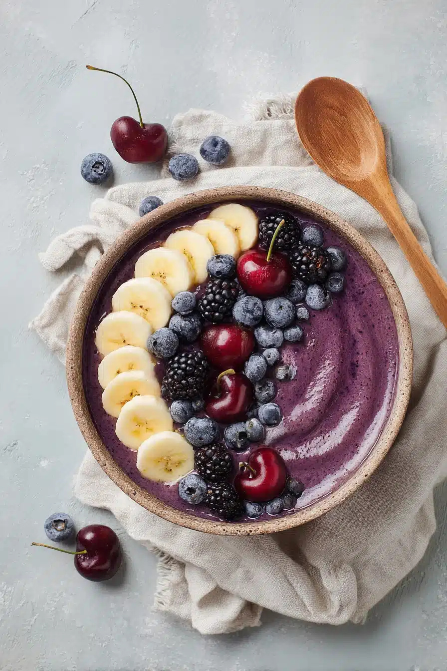 Cherry berry smoothie bowl with banana slices, blueberries, and blackberries on light background