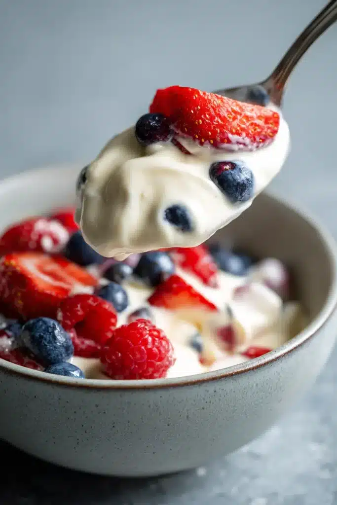 Spoon lifting red white and blue cheesecake salad with strawberries, blueberries, and creamy filling
