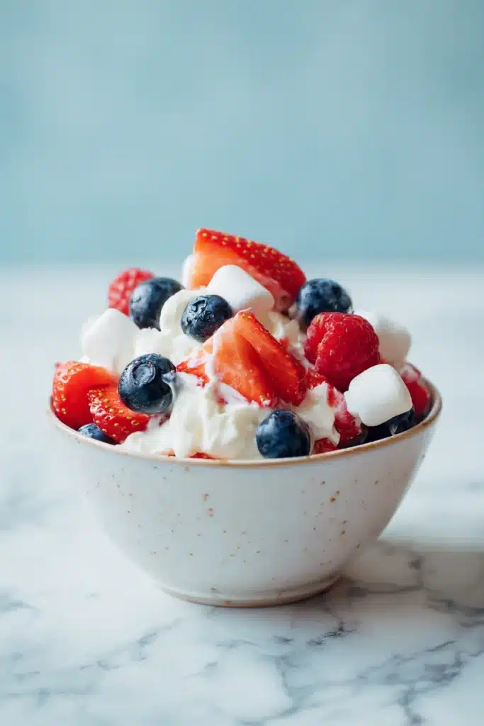 Red white and blue cheesecake salad with strawberries, blueberries, and creamy filling in a bowl