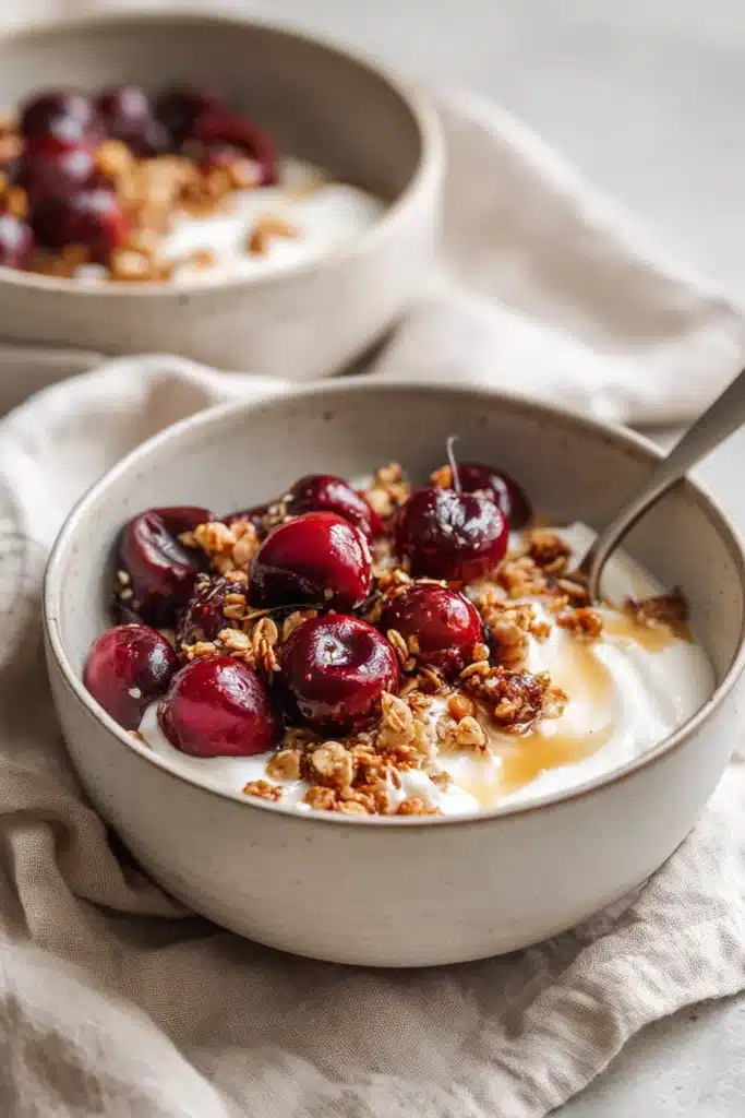 Roasted cherry yogurt bowl with granola and honey drizzle in ceramic bowl