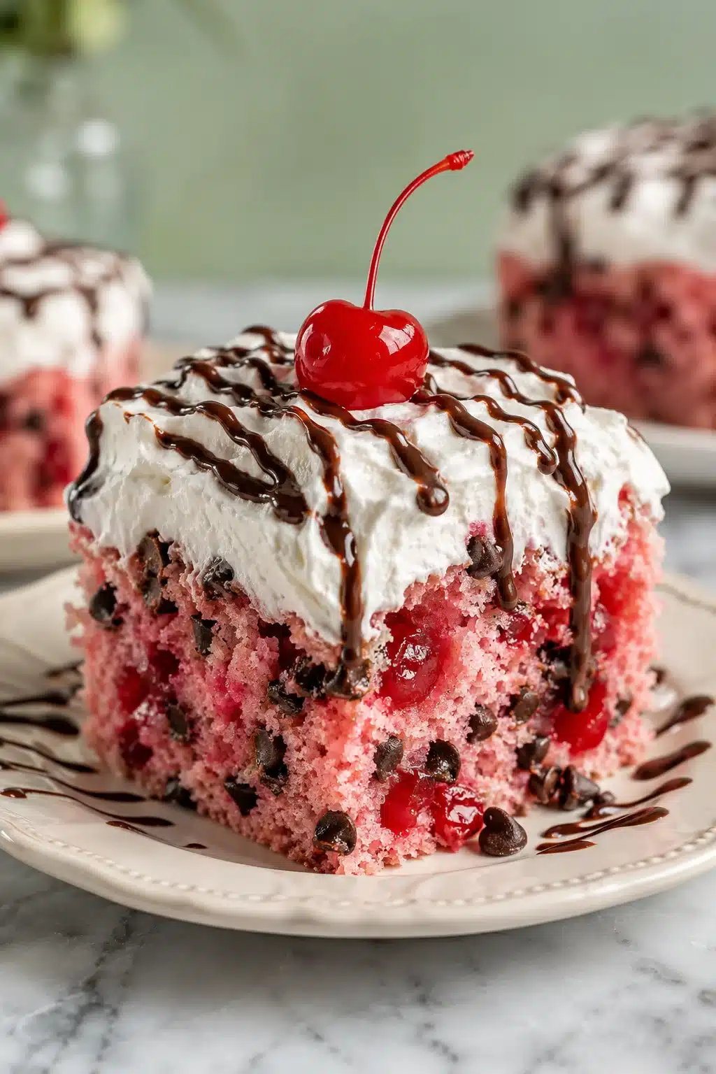 Cherry Chocolate Chip Poke Cake slice with whipped topping, chocolate drizzle, and cherry garnish