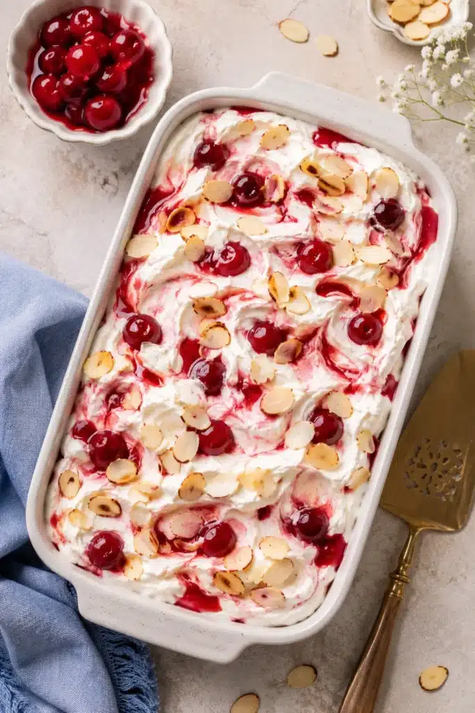Overhead Heaven On Earth Cake with cherry pie filling, whipped topping, and toasted almonds in a baking dish.